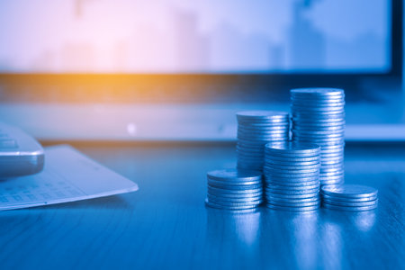 Coins stacked on each other and laptop computer background, business and finance conceptの写真素材