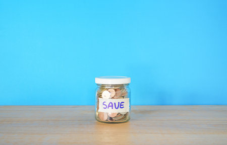Coins in the glass jar with save word on blue background.の写真素材