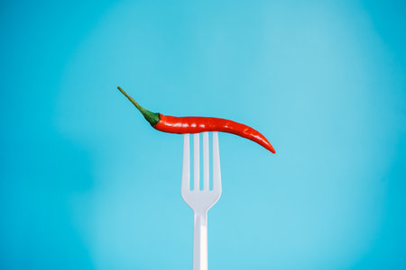 Red hot chili pepper on a fork on a blue background with copy spaceの写真素材
