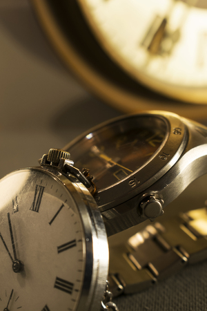 Old pocket watch and modern watch in close-up view with old wall clock in background