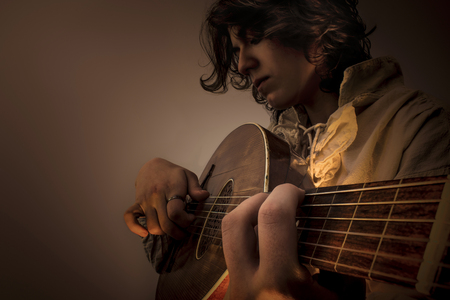 Young man with long blond hair sitting in dark environment and playing an Old Oud, Guitar Lute and...