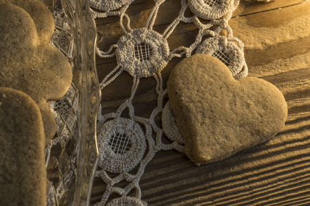 Cookies on Knitted tablecloth and wooden table. Two of them is white with powdered sugar and one with shape of heartの写真素材