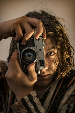 Young boy with long blond hair dressed in sweater. He holding an old russian camera in his hands, and taking a shotの写真素材