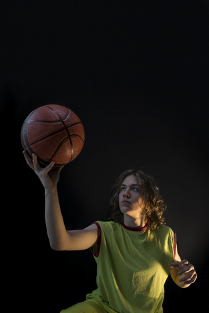 Young boy with long blond hair wearing a green jersey looking determinedly at the basket ball.の写真素材