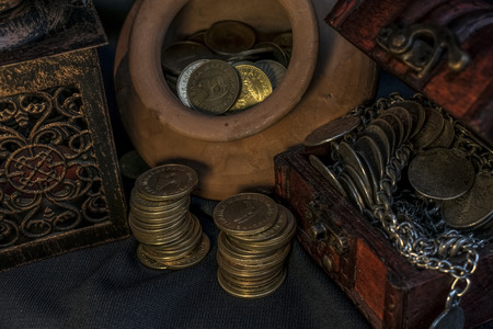Treasure chest, pile and pillar of coins, a ceramic bowl filled with jewelry coins and candle lamp in dark environmentの写真素材