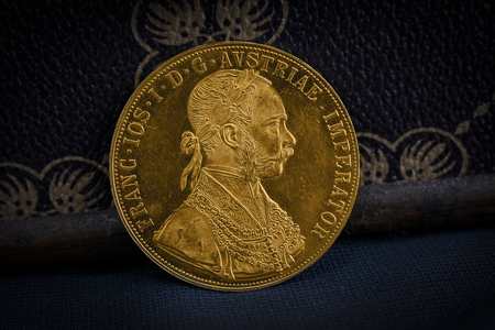 Close-up view of Austria-Hungary thaler, avers of golden coin-ducat from 1915 with Kaiser Franz Joseph I, leaning on treasure chest and dark environmentの写真素材