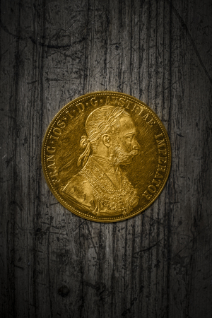 Close-up view of Austria-Hungary thaler, avers of golden coin-ducat from 1915 with Kaiser Franz Joseph I on dark wooden backgroundの写真素材