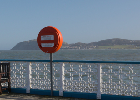 Red lifebuoy with sea and mountains in background on pierの写真素材