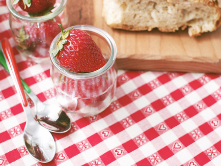 Picnic stil life with bread on wooden cutting board and strawberrie in glass cups on red checkered table clothの写真素材