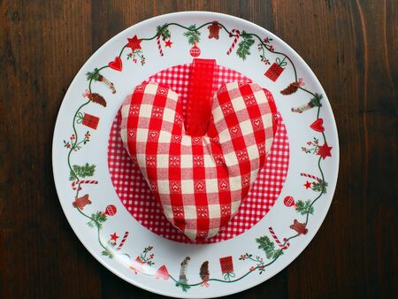 Soft checkered stuffed heart in canvas on christmas plate and on brown wooden tableの写真素材