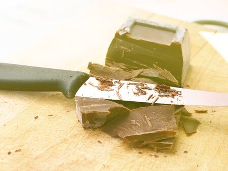 Bitter chocolate being cut and shredded for a dessert on wooden boardの写真素材
