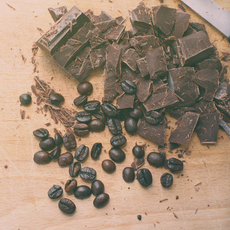 Shredded dark chocolate with coffe beans on wooden chopping board, toned, top view and square size