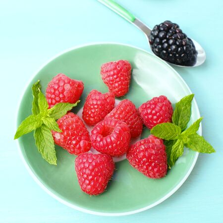 Raspberries on a green pastel plate decorated with mint, square