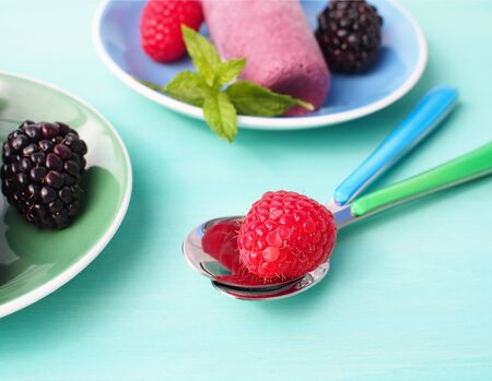 Raspberry on a spoon with home made ice cream behind with raspberries and blackberries, decorated...