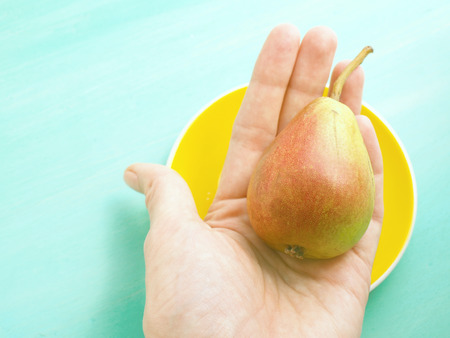 Pear in a hand on green pastel wooden backgroundの写真素材