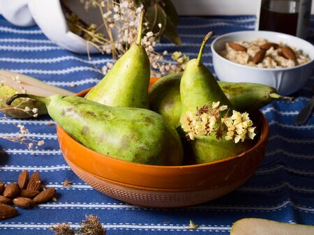 Rustic bowl with green pears on blue table cloth with almonds, honey, oatmeal porridge and dried flowers around, fruit still lifeの写真素材