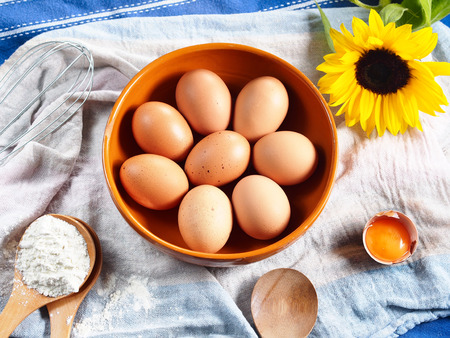Baking still life with eggs in a clay bowl, egg whisk, spoons with flour and a sunflower on rustic background. spring motivesの写真素材