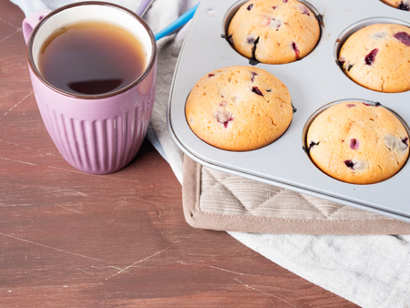 Just baked muffins in a muffin tin with a cup of tea on wooden table, copy spaceの写真素材