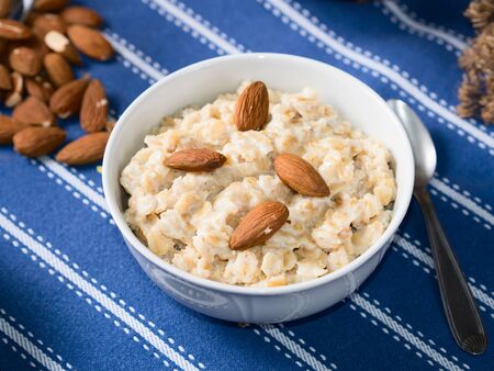 Oatmeal porridge with pears, honey and almonds for breakfast on dark blue table clothの写真素材