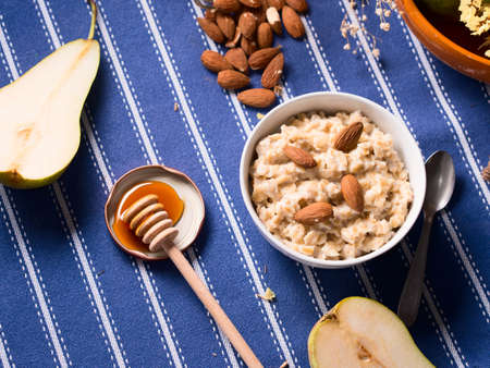 Oatmeal porridge with pears, honey and almonds for breakfast on blue table clothの写真素材