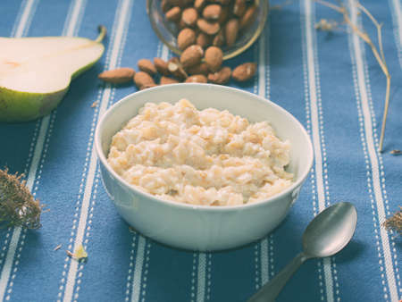 Oatmeal porridge with pears, honey and almonds for breakfast on blue table clothの写真素材