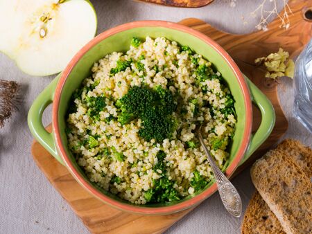Millet porridge with broccoli in a green bowl on beige table clothの写真素材