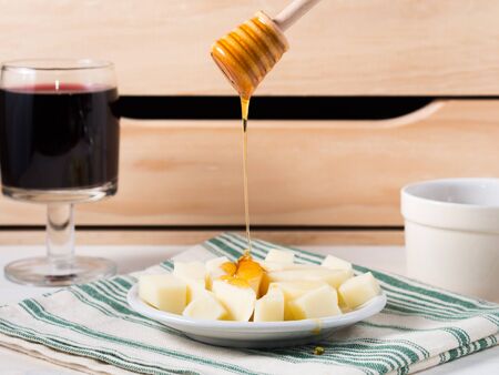 Pouring honey on pieces of cheese on a plate with wine and  honey in the backgroundの写真素材
