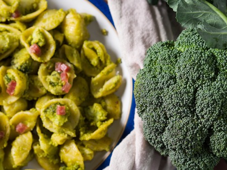 Fresh raw broccoli with orecchiette pasta with broccoli, bacon and parmesan in the backgroundの写真素材