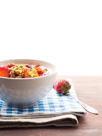 Smoothie bowl with yogurt, strawberries, dried fruit, pistachio nuts, raisins and chia seeds on checkered napkin and wooden table, copy space. Vertical shotの写真素材