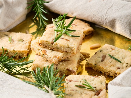 Butter cookies with rosemary, pignoli and pistachio nuts on golden tray, decorated with rosemary sprigsの写真素材
