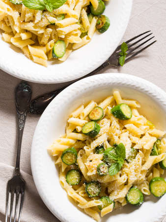 Pennette pasta with zucchini, fresh mint and grated parmesan cheese on beige table cloth, vertical shotの写真素材