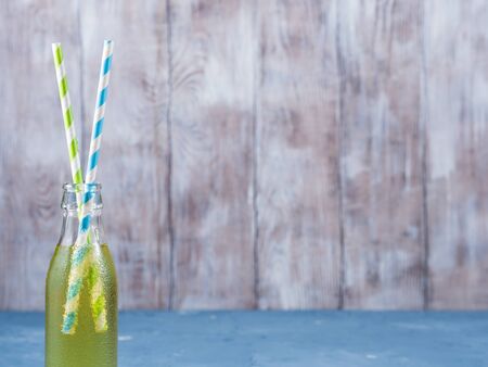 Lemon sparkling soft drink in a glass bottle with colored paper straws on wooden background with copy spaceの写真素材