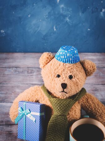 Christmas background on rustic wooden board with a vintage teddy bear with a vintage tie, gift box and mug of coffee. Copy space. Vertical imageの写真素材