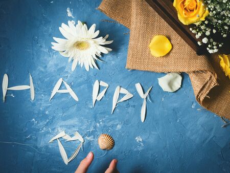 Word happy written with petals of a gerber on blue textured background with floral composition...