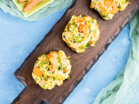 Baked vegetable patties with carrots, broccoli and cheese on dark wooden serving boardの写真素材
