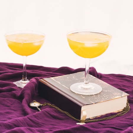 Two orange alcohol cocktails on purple textile with a bookの写真素材