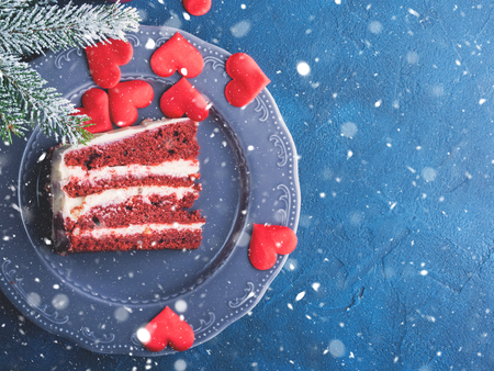 Red velvet cake slice for Valentines day dessert. Sweet treat for romantic date or Christmas party. Holiday celebration dark blue and black background with winter fir tree branches.の写真素材