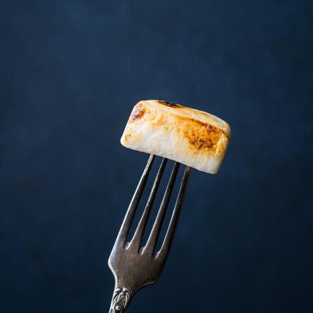 Smoked marshmallow on vintage fork on dark background. Minimal still life on blackの写真素材