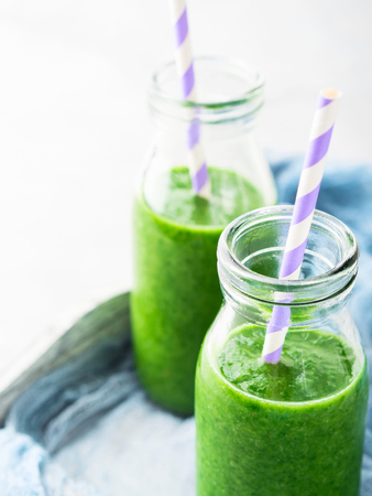 Healthy food concept green smoothie breakfast on white gray tray blue textile. Fruit vegetable juice glass bottleの写真素材