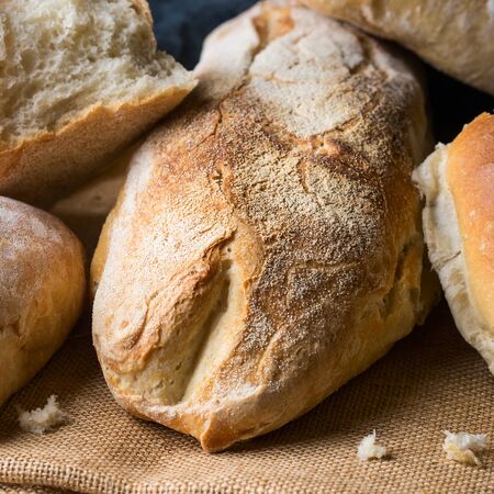 Freshly baked bread loaves on burlap dark wooden background. Texture closeup italian bakery...