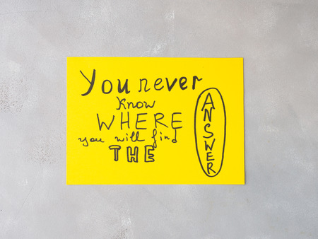 Yellow card spelling hand written words You never know where you will find the Answer on gray...