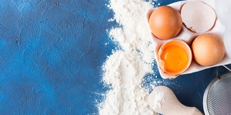 Baking tools rolling pin whisk and ingredients flour egg, sugar on dark blue background. top view flat lay. Making dough for cookies cake pie process concept bannerの写真素材