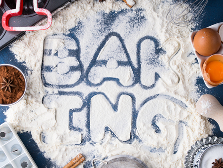 Flour letters spelling Baking with tools and sweet food ingredients sugar, eggs, cocoa, cinnamon. Top view flat lay conceptの写真素材