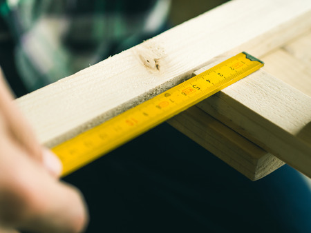 Man crafting wooden chair object keeping wooden boards in hands. Measuring with meter tool. Do it yourself project making processの写真素材