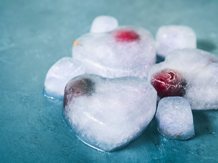Heart shaped lavender syrup ice cubes with frozen cherry on blue textured background. Tonedの写真素材