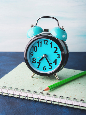 Alarm clock and businessman's accessories on blue background. Office manager morning concept with tie, notebook, stationeryの写真素材