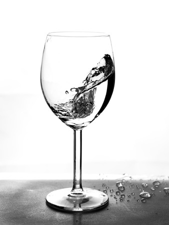 Half empty glass with water splashes in motion on white background.の写真素材