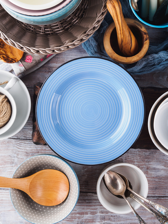 Ceramic and enamel crockery tableware on wooden background. Pastel vintage colors. Blue empty plate for textの写真素材