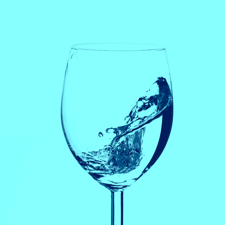 Half empty glass with water splashes in motion on white background.の写真素材