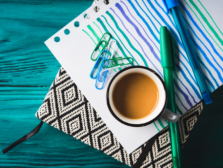 Cup of coffee, notebook and pens on dark green wooden background. Winter mood backdrop